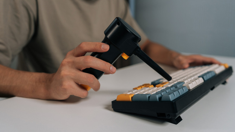 Man using an electric air duster to clean a keyboard