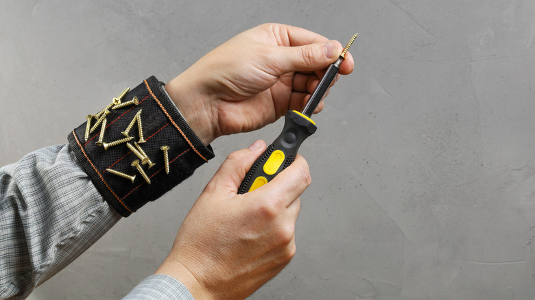 Man with a screwdriver and some screws magnetically stuck on a wristband