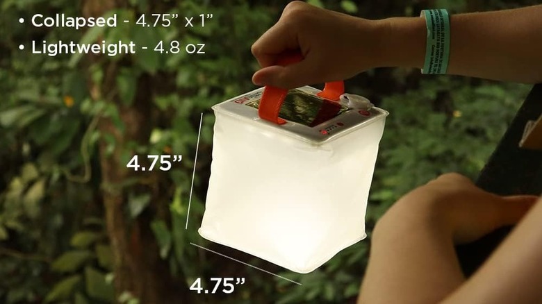 Hand holding a LuminAID lantern in dark conditions, with writing stating the dimensions and weight of the lantern
