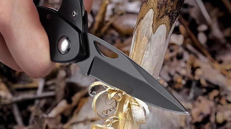 Hand holding a multitool carabiner and cutting a twig with the pocket knife tool