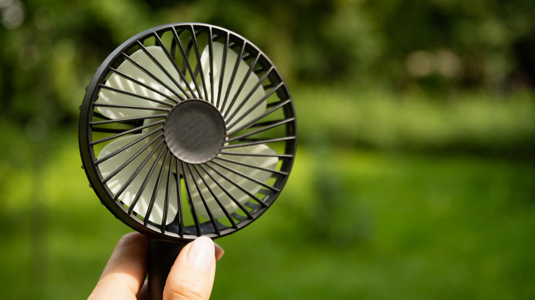 An electric portable fan held in a person's hand outdoors