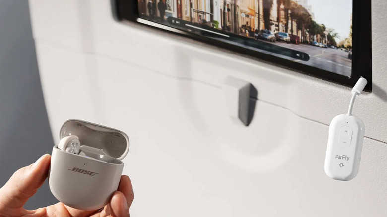 The Twelve South AirFly Pro 2 attached to an airplane's entertainment system, with a person holding a pair of Bose earbuds in front of it