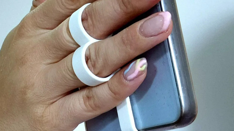 A person with manicured nails holding a smartphone with the aid of a finger ring holder
