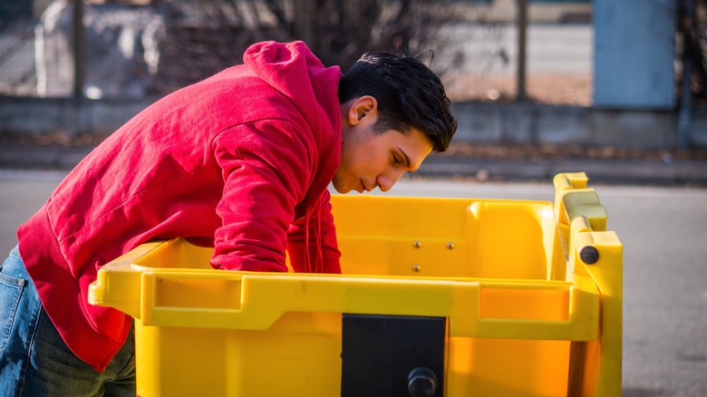 A man dumpster diving in a yellow trash bin