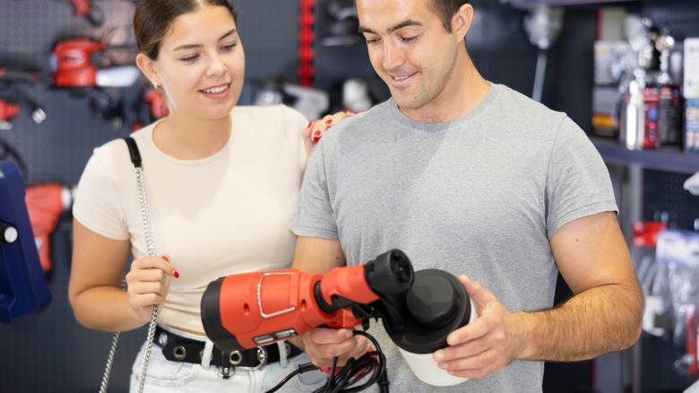 A couple examining an open paint sprayer in a hardware store
