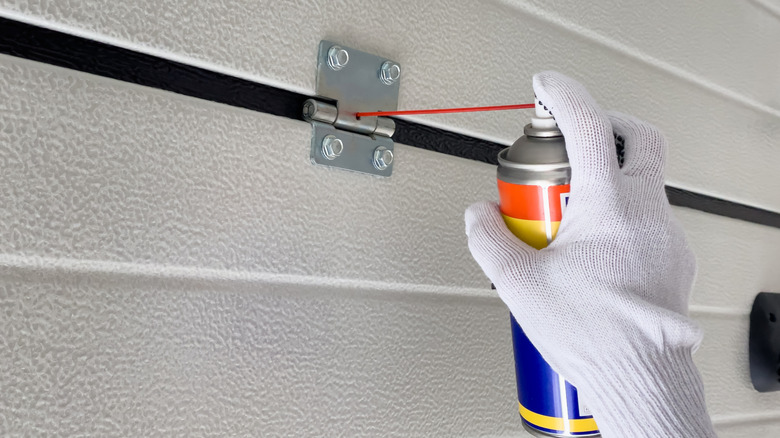 A person spraying WD-40 on a garage door hinge
