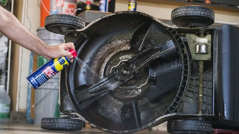 Person spraying WD-40 on lawn mover blades