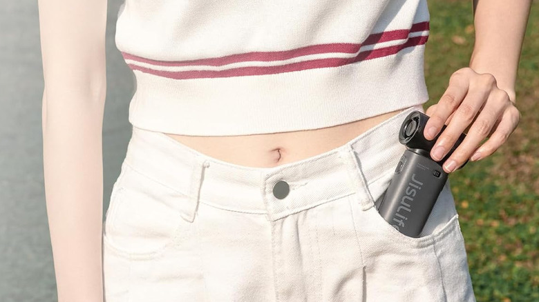 A person putting the Jisulife portable handheld fan into their trouser pocket