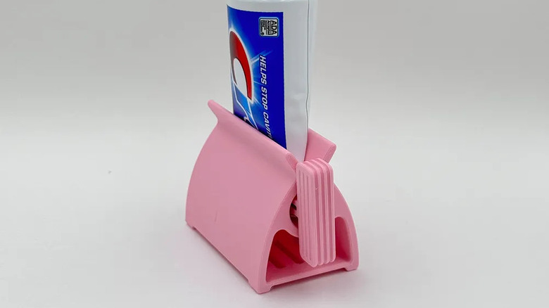 pink toothpaste squeezer with a tube of toothpaste inserted and halfway squeezed