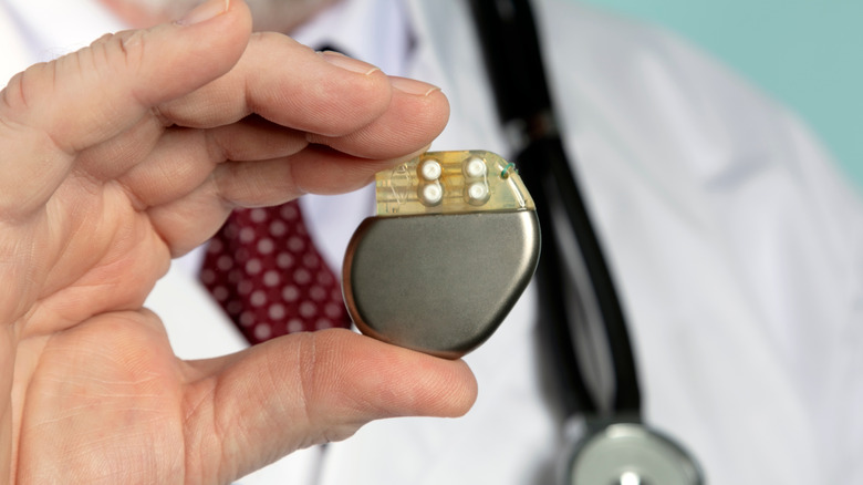 A doctor holding a pacemaker in front of their chest