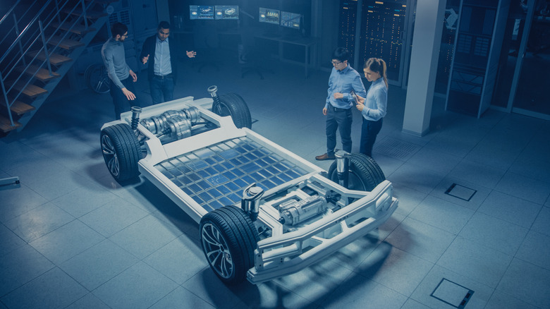 A group of plant employees around a bare EV car chassis