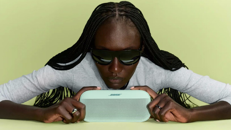 A person wearing shades and holding the Bose SoundLink Flex (2nd Gen) in front of a lime-green background