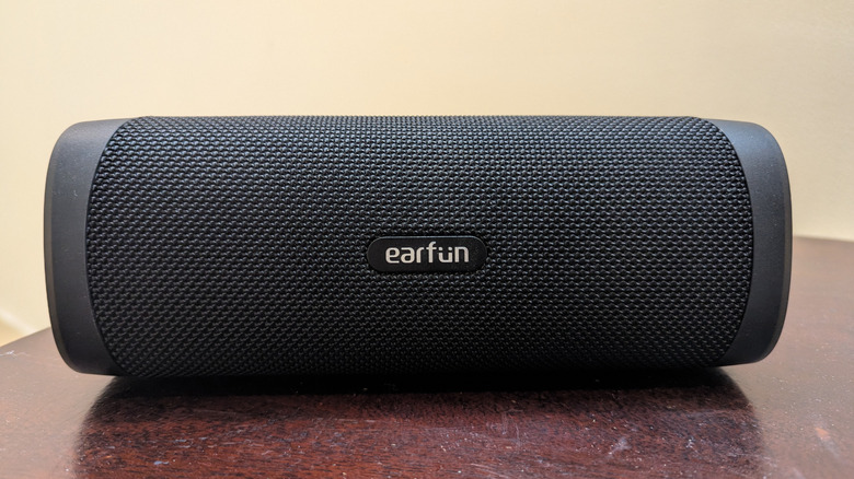 The EarFun UBOOM L speaker placed on a wooden table in front of a cream-colored wall