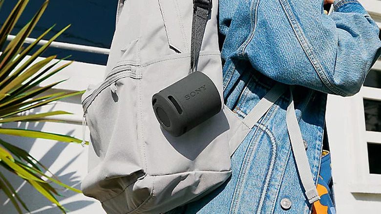 The Sony SRS-XB100 speaker hooked onto the bag of a person wearing a denim jacket