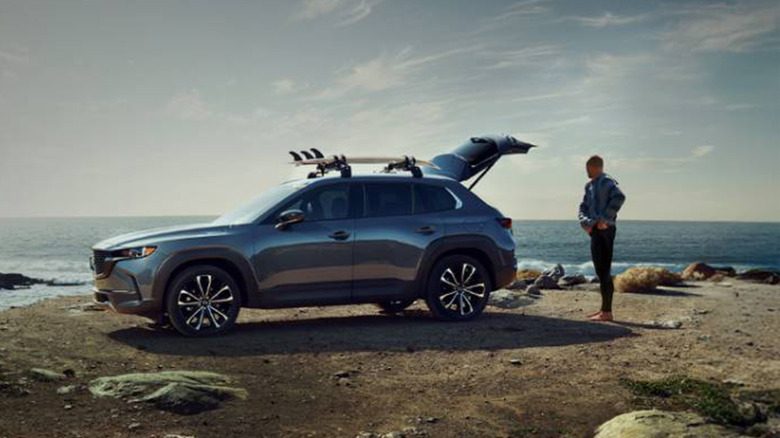 A Mazda CX-50 and its owner by a seaside rocky area