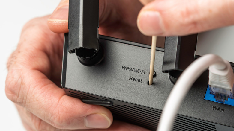 A reset button being pressed on the back of a router