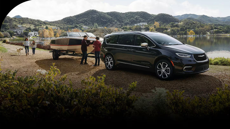 A Chrysler Pacifica towing a boat with a family near a lake.