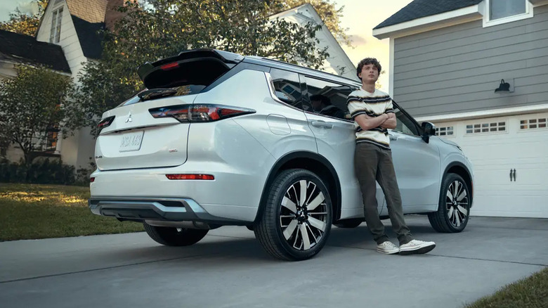 A man standing against a white Mitsubishi Outlander.