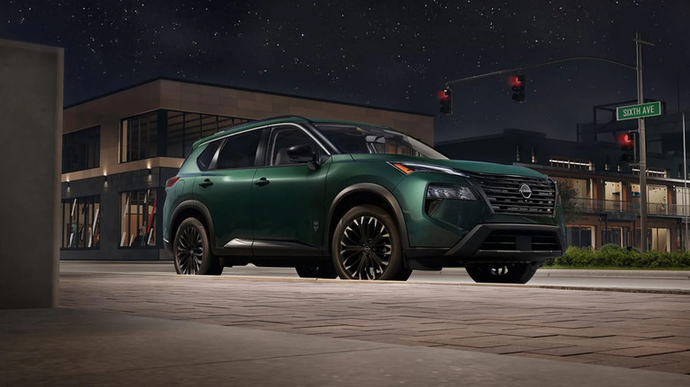 A green Nissan Rogue on a city street at night.