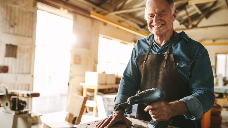 older man holding a drill in workshop