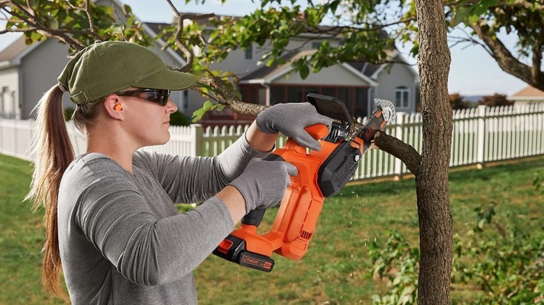 Woman using a pruning chainsaw to cut a tree branch.