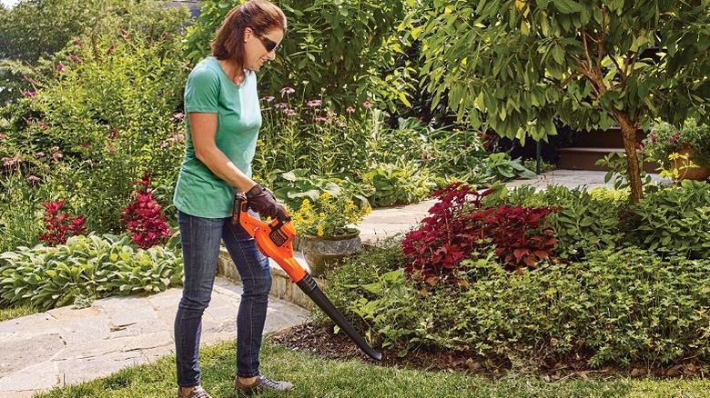Woman using a leaf blower to remove fallen leaves.