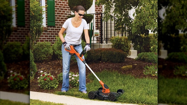Woman using a mower to shape the grass along sidewalks.