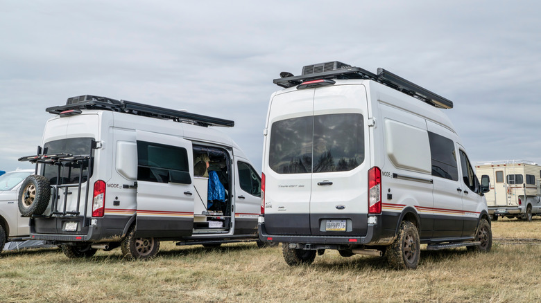 Two overland build camper vans both based on the Ford Transit chassis parked next to each other in a field.