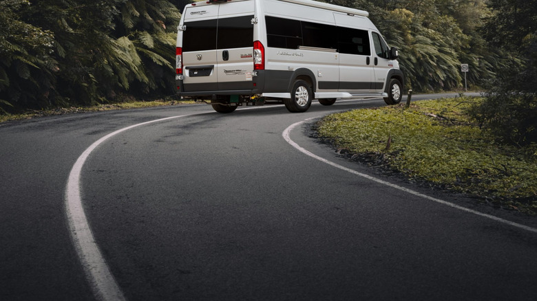 A white Pleasure Way 2025 Lexor TS camper van making its way down a forested road