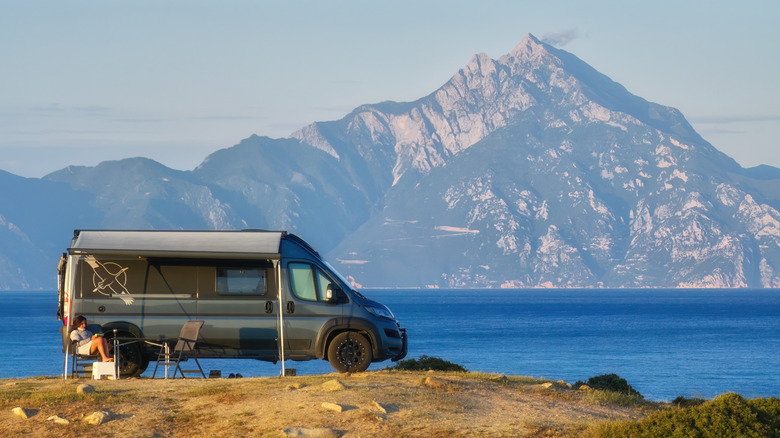 A camper van finished in grey parked by the sea with a mountain in the backgroud
