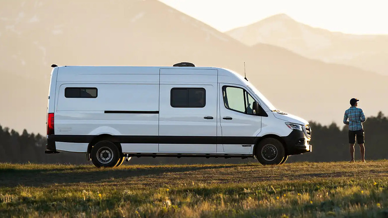 A white Winnebago plus adventure wagon parked in a field, side view visible