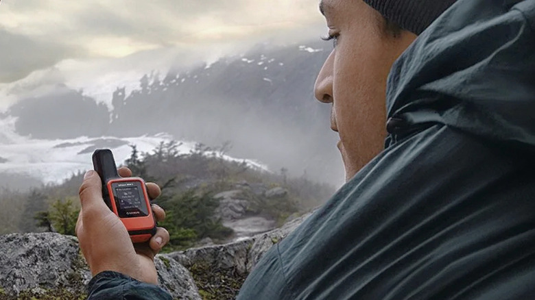 A man using the Garmin inReach Mini 2 while hiking in the mountains.
