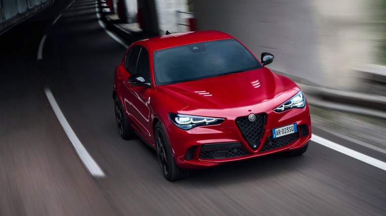 a red Alfa Romeo Stelvio driving out of a mountain pass