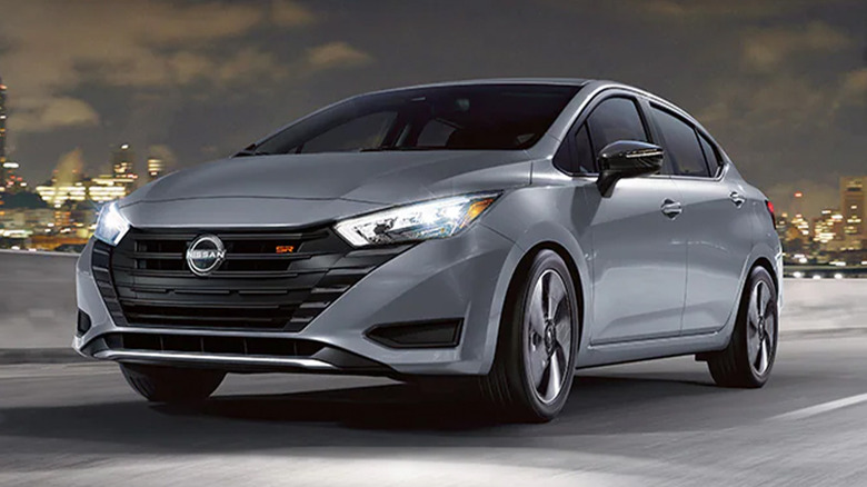 A gray Nissan Versa on a highway with a cityscape in the background
