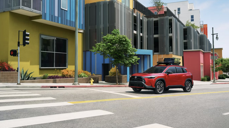A red Toyota Corolla Cross SUV at a stop light in a colorful town