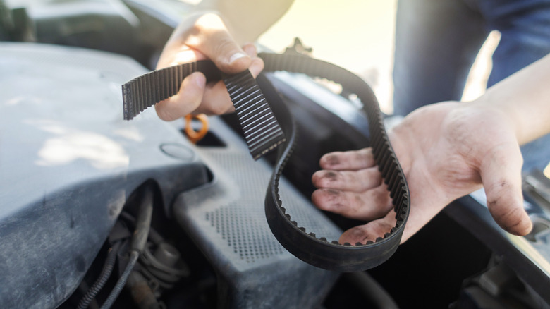 Mechanic holding a broken driving belt over an engine