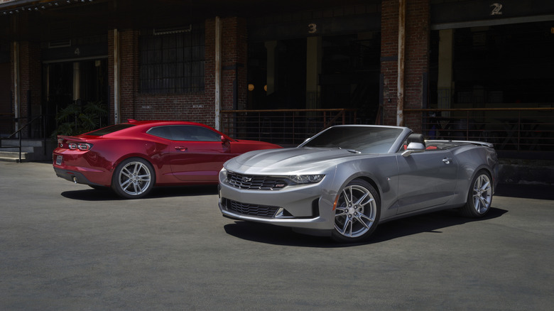 A silver Camaro convertible standing next to a red Camaro coupe, both models being for the 2023 model year.