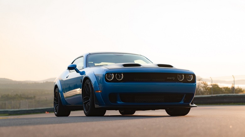 A low-down view of a Dodge Challenger vehicle from the last generation standing on a racetrack against the sun.