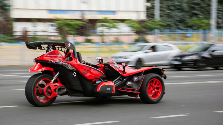 A red and orange Polaris Slingshot Autocycle photographed at speed on a public road.