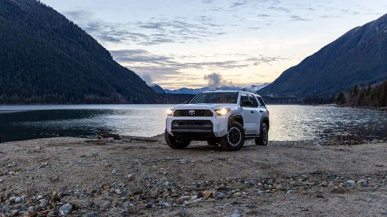 A white Toyota 4Runner off-roading beside a body of water with mountains in view