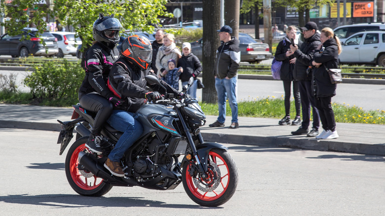 A black Yamaha MT-03 with orange spoked wheels being ridden through a side street.
