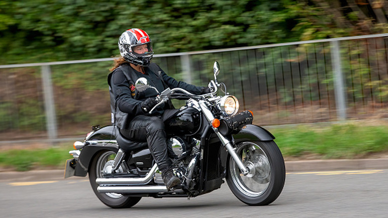 A rider in a jacket and helmet on a black and silver Honda Shadow cruising along a road.