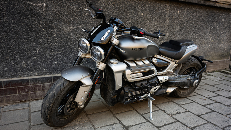 A sleek, metallic Triumph Rocket III with its signature dual headlights parked next to a textured wall.
