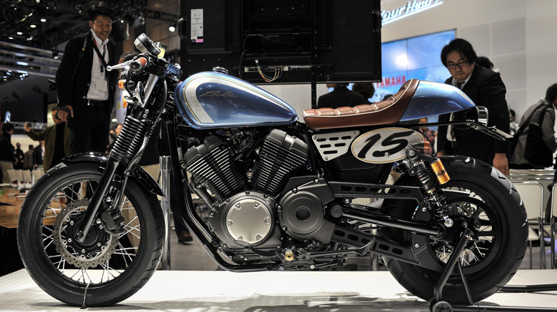 A Yamaha Bolt in a Cafe Racer edition on display during an indoor show in Tokyo, with people looking at it.