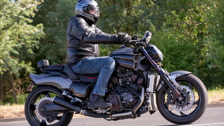 A rider in full gear on a 2015 Yamaha VMAX muscle cruiser moving left to right on a small road.