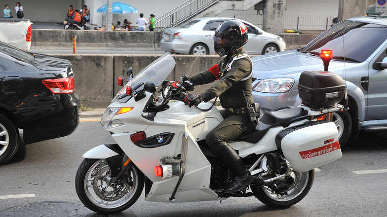 A traffic police officer riding a white BMW K1300 GT while in traffic.