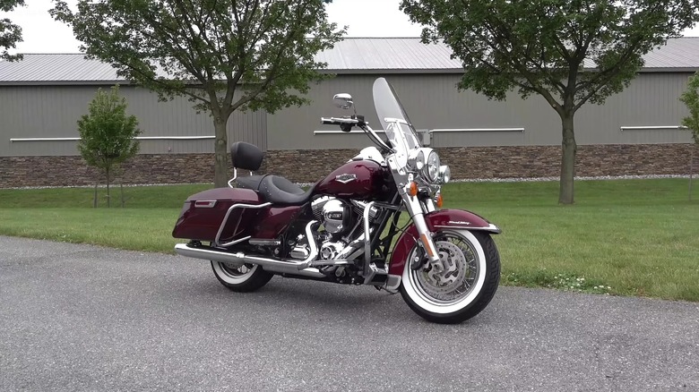 A burgundy chromed Harley-Davidson Road King from 2010 next to some trees.