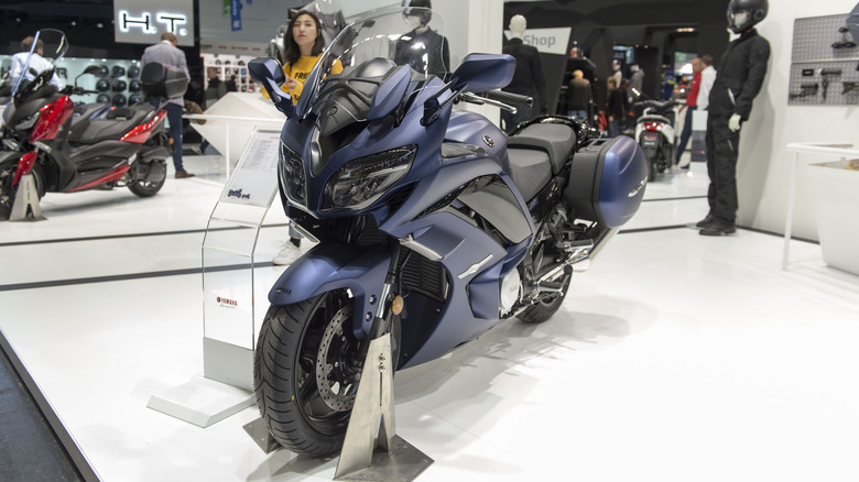 A blue Yamaha FJR1300 AE displayed on a podium at a trade show.