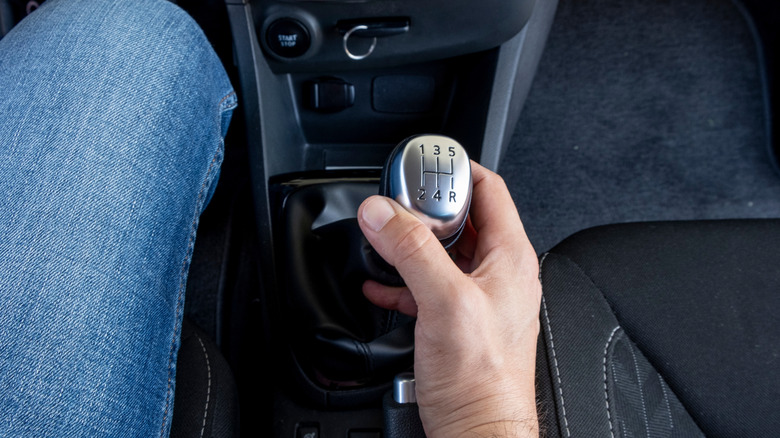 A person's hand gripping a manual gear shifter in a car.