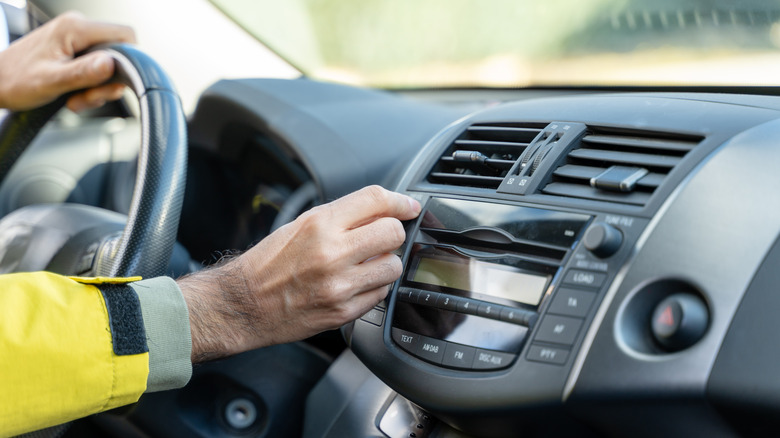 A driver adjusts the manual air vent in a car's dashboard, with a close-up view of the center console.